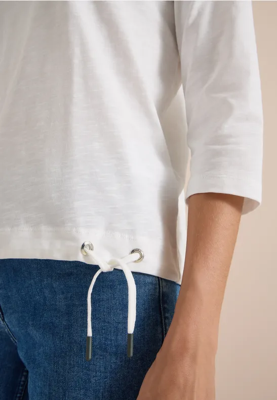 Gros plan sur un t-shirt blanc à manches 3/4 avec cordon et un jean bleu.