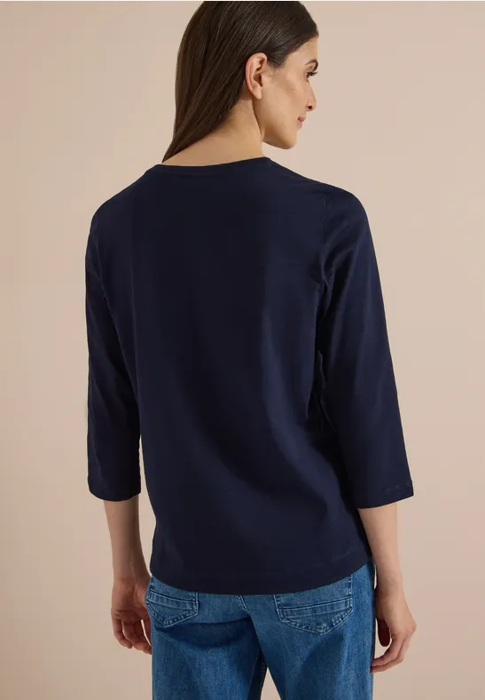 Vue de dos d'une femme portant un T-shirt bleu marine à manches 3/4 et un jean.