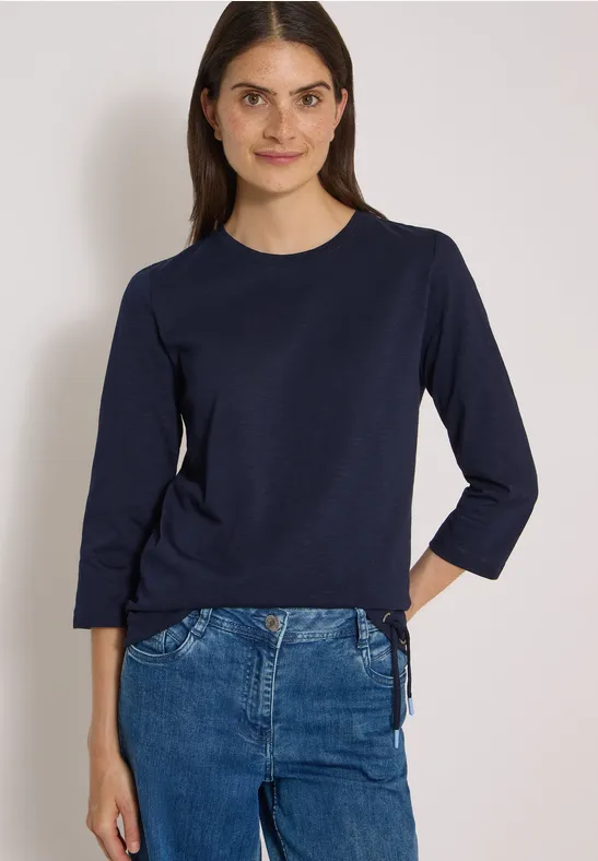 Femme portant un t-shirt bleu marine à manches trois-quarts avec laçage latéral et un jean.