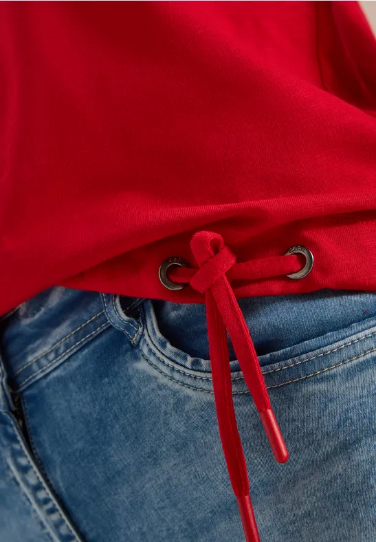 Roter Pullover mit Tunnelzug am Saum, kombiniert mit blauen Jeans.