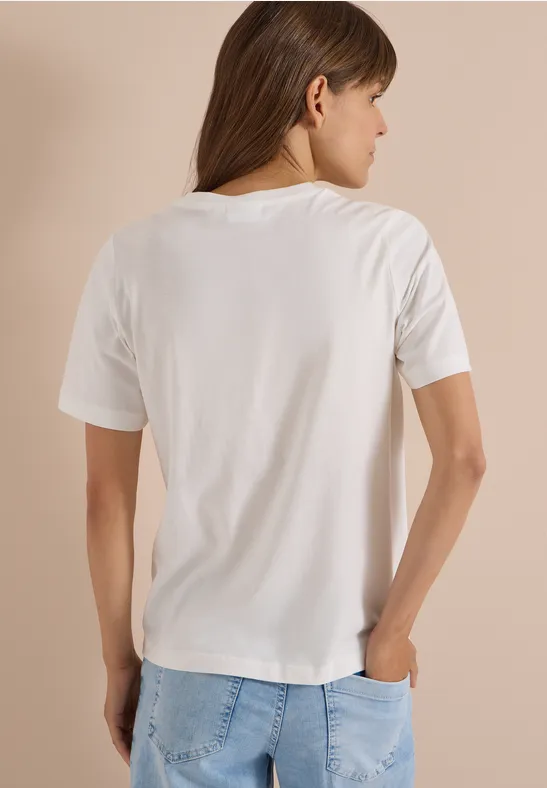 Frau von hinten in weißem T-Shirt und Jeans vor neutralem Hintergrund.