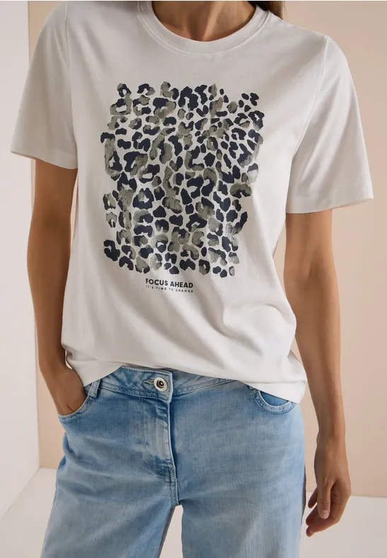 Frau in weißem T-Shirt mit Leopardenmuster und blauer Jeans.