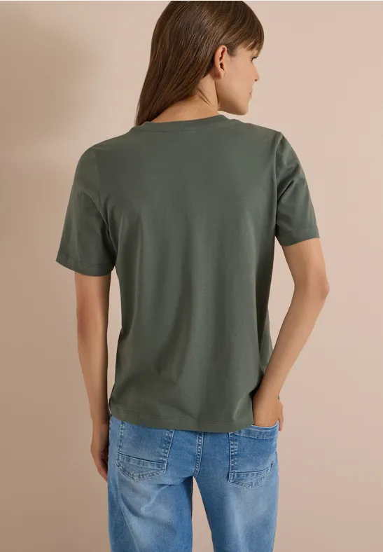 Eine Frau ist von hinten zu sehen, sie trägt ein olivgrünes T-Shirt und eine blaue Jeans.