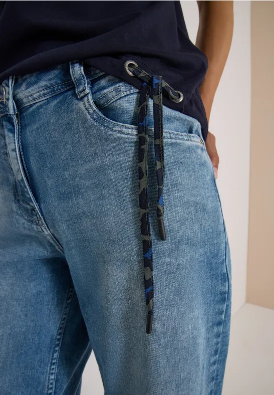 Lockere blaue Jeans mit Kordelbund und Hand in Tasche.