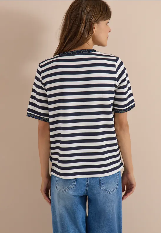 Rückenansicht einer Frau in blau-weiß gestreiftem T-Shirt und lockeren Jeans vor beigem Hintergrund.