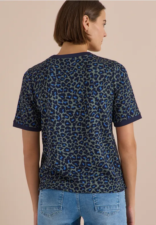 Frau steht von hinten, trägt blau-grünes Leo-Shirt und Jeanshose.