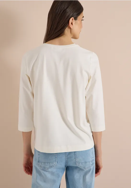 Achteraanzicht van een vrouw met wit shirt met driekwart mouwen en blauwe jeans tegen lichte achtergrond.