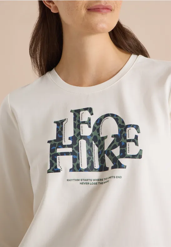 Vrouw draagt wit T-shirt met grote 'LEGO HIKE'-opdruk in camouflagepatroon.