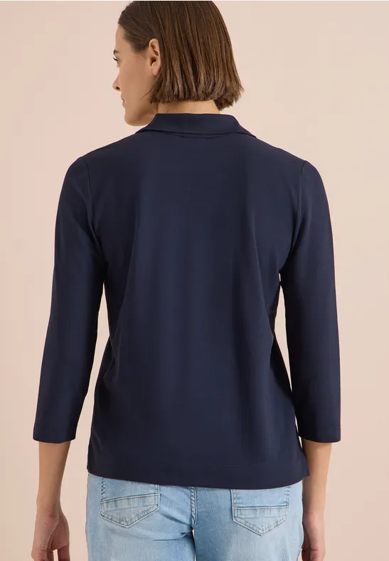 Rückansicht einer Person in dunkelblauem 3/4-Ärmelshirt und heller Jeanshose.