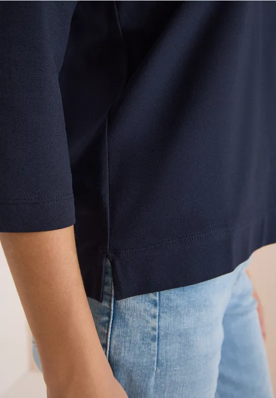 Seitliche Ansicht einer Person mit marineblauem Shirt mit 3/4-Ärmeln und hellblauen Jeans.