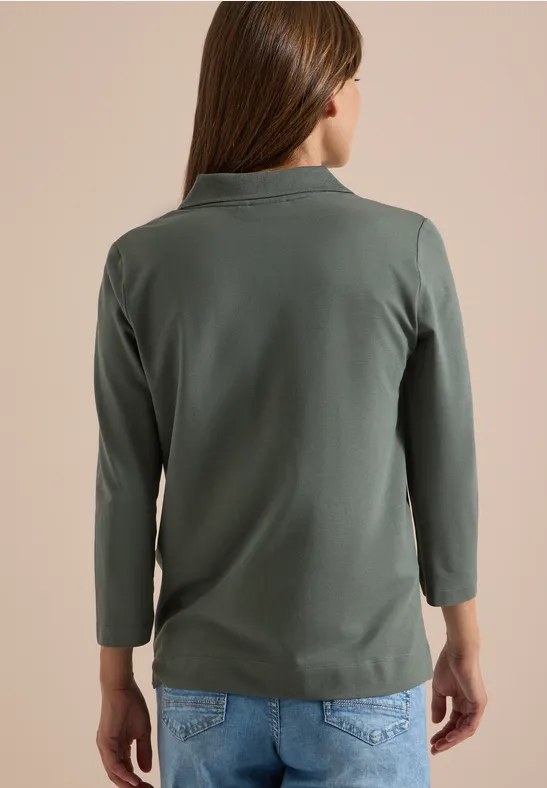 Frau von hinten in olivgrünem Langarmshirt mit Stehkragen und blauen Jeans.