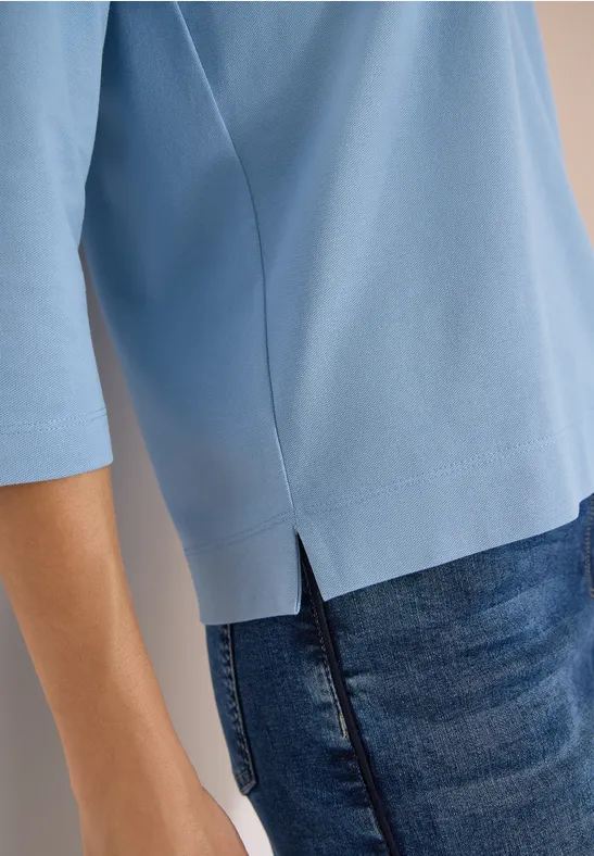 Person trägt hellblaues Shirt mit 3/4-Ärmeln und seitlichem Saumschlitz, kombiniert mit dunkler Jeans.