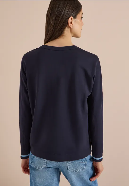 Achteraanzicht van een vrouw met een donkerblauw shirt met lange mouwen en een spijkerbroek voor een lichte achtergrond.