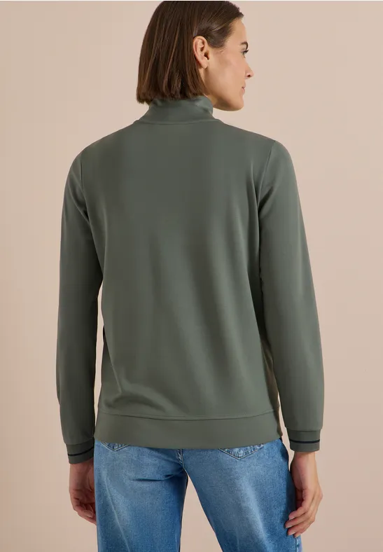 Frau von hinten in grau-grünem Rollkragenpullover und Jeans.
