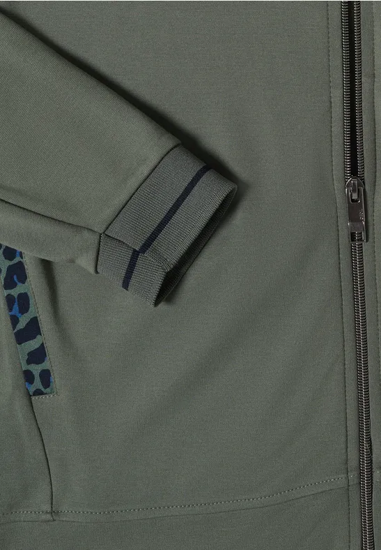 Nahaufnahme einer grau-grünen Jacke mit Reißverschluss, elastischem Ärmelbündchen und gemustertem Taschenbesatz.