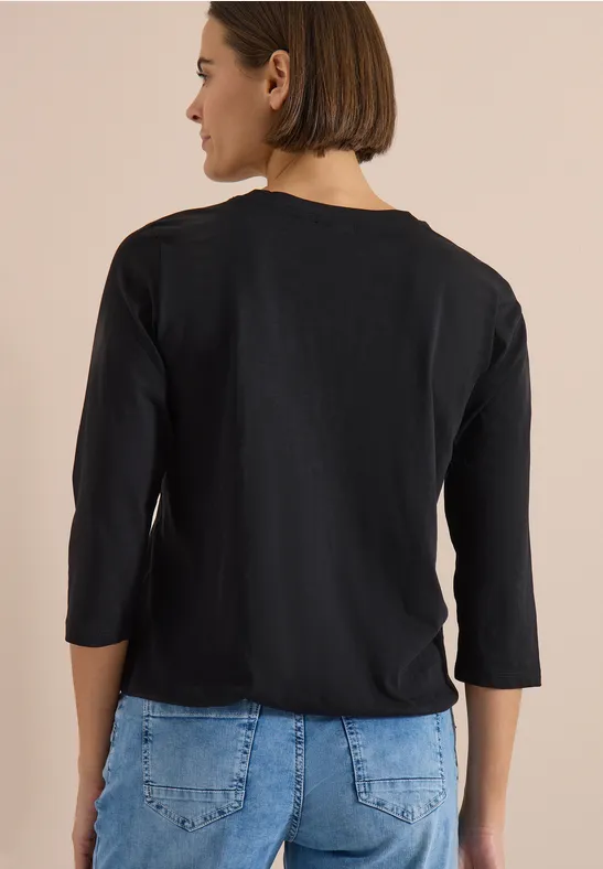Rückenansicht einer Person mit kurzem Bob, schwarzem 3/4-Shirt und blauen Jeans.