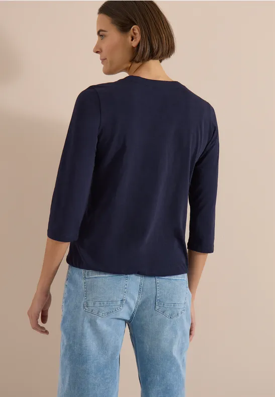 Person von hinten in marineblauem 3/4-Shirt und hellblauen Jeans.
