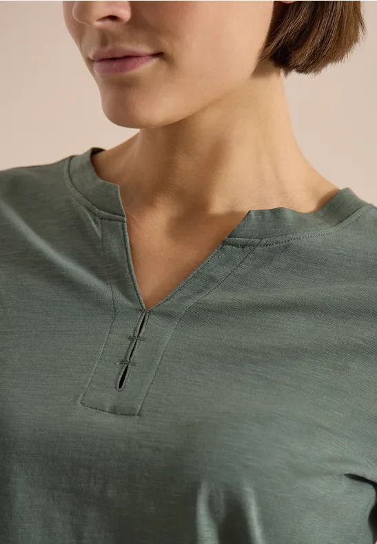 Nahaufnahme einer Frau im grünen T-Shirt mit V-förmigem Ausschnitt und Knopfdetail.