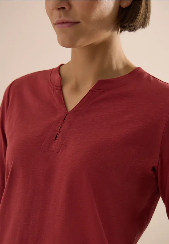 Frau trägt langärmliges rotes Shirt mit V-Ausschnitt und verdeckter Knopfleiste.