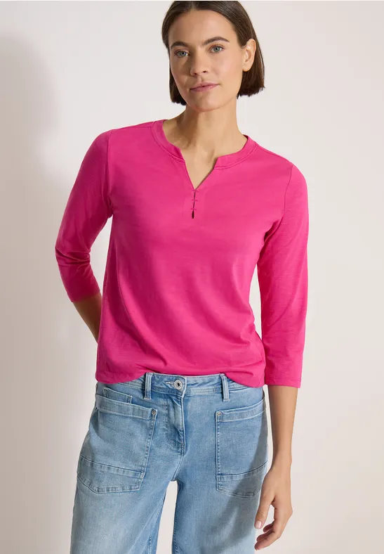Frau trägt pinkes 3/4-Arm-Shirt mit V-Ausschnitt und blaue Jeans.