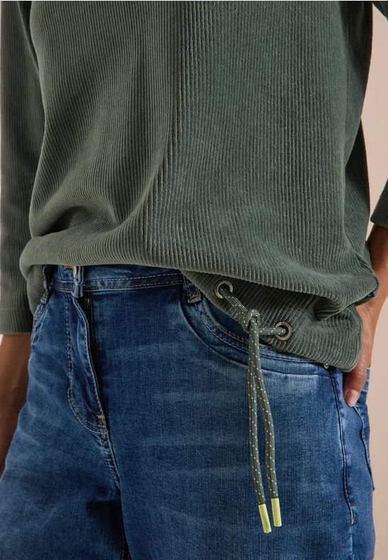 Jeans mit grünem Tunnelzug und passendem grünen Pullover, Hand in Tasche.