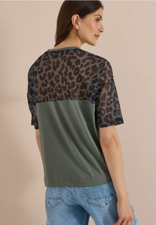 Vrouw van achteren in T-shirt met transparant luipaardprint bovenstuk en olijfgroen onderstuk.
