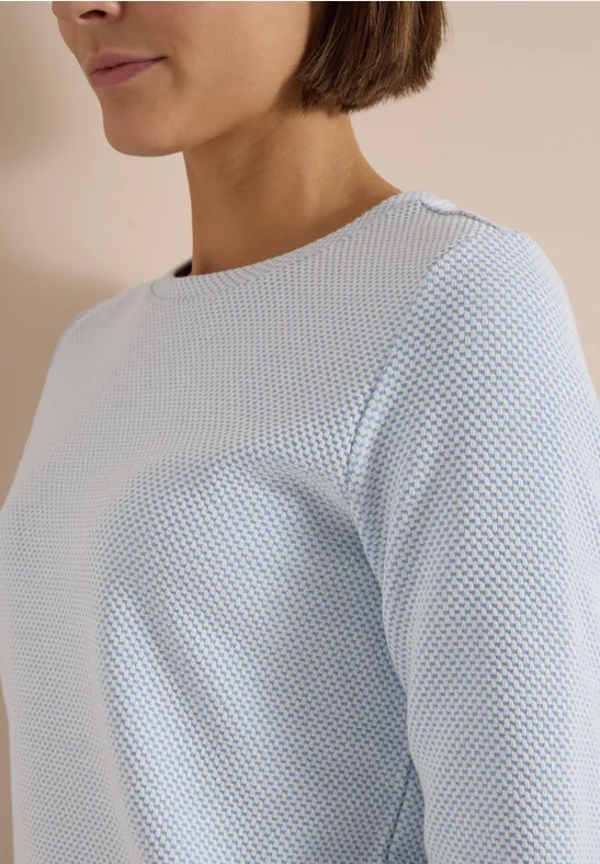Eine Frau trägt ein hellblaues, strukturiertes Langarmshirt.