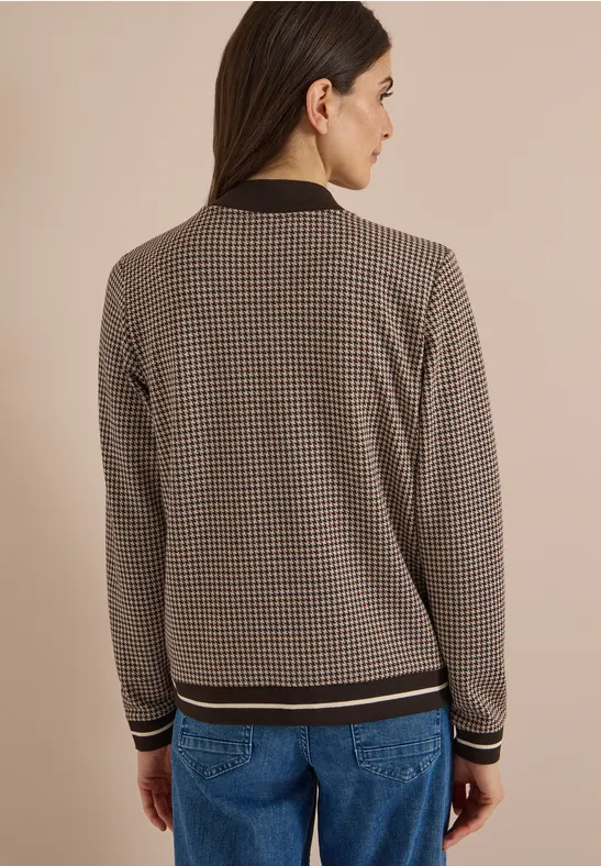 Rugaanzicht van een vrouw in spijkerbroek en getailleerde gebreide cardigan met geruit patroon.