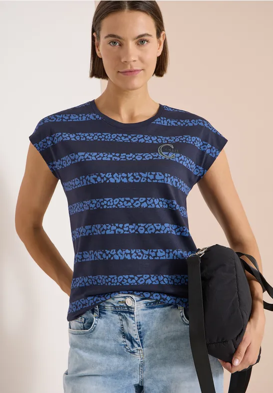 Frau in blau-schwarz gestreiftem T-Shirt, Jeans und Rucksack vor neutralem Hintergrund.