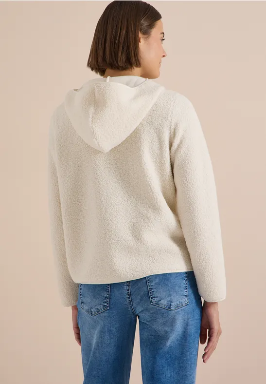 Frau von hinten in weißem Kapuzenfleece mit weichem Teddy-Material, kombiniert mit blauen Jeans.