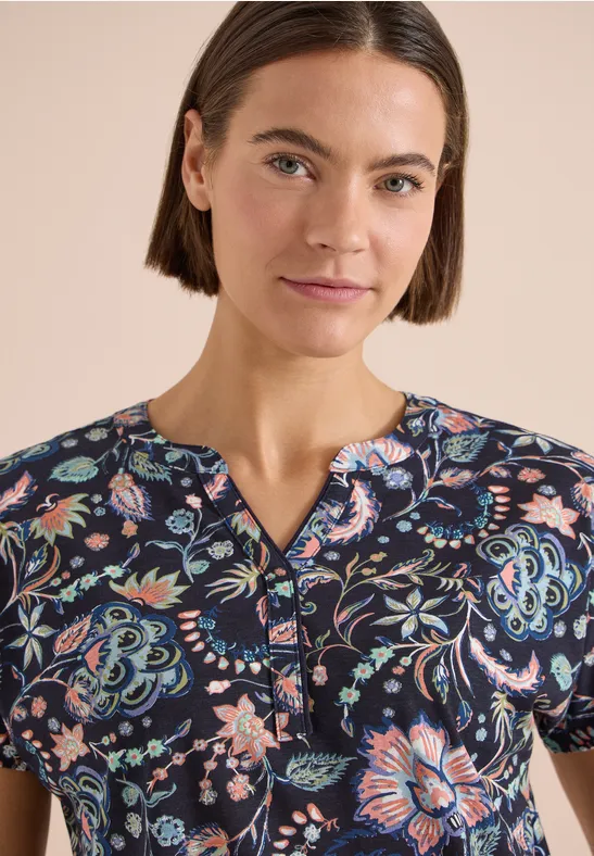 Frau trägt kurzärmliges, dunkelblaues Oberteil mit buntem Blumenmuster und V-Ausschnitt.