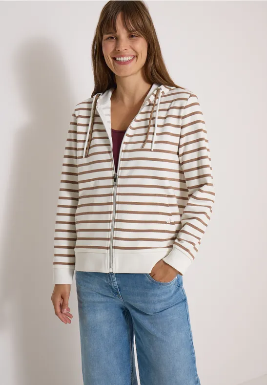 Eine Frau trägt eine gestreifte Kapuzenjacke mit Reißverschluss und hellen Jeans.