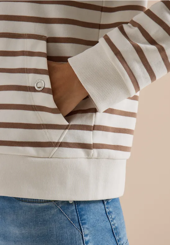 Nahaufnahme eines Oberkörpers in beigebraun gestreiftem Pullover mit Hand in der Tasche und Jeans.