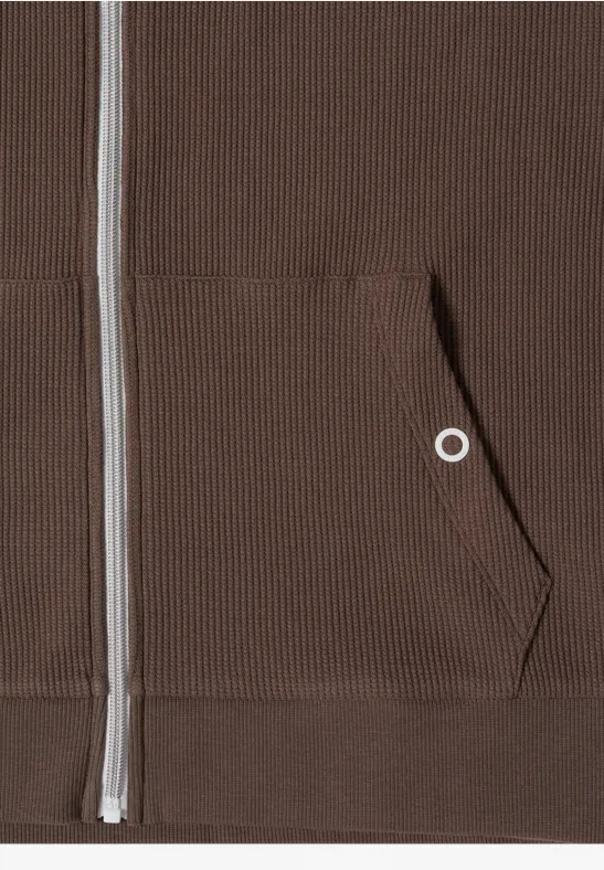 Close-up van een bruin sweatjack met rits, kangoeroezak en geribbelde stof.