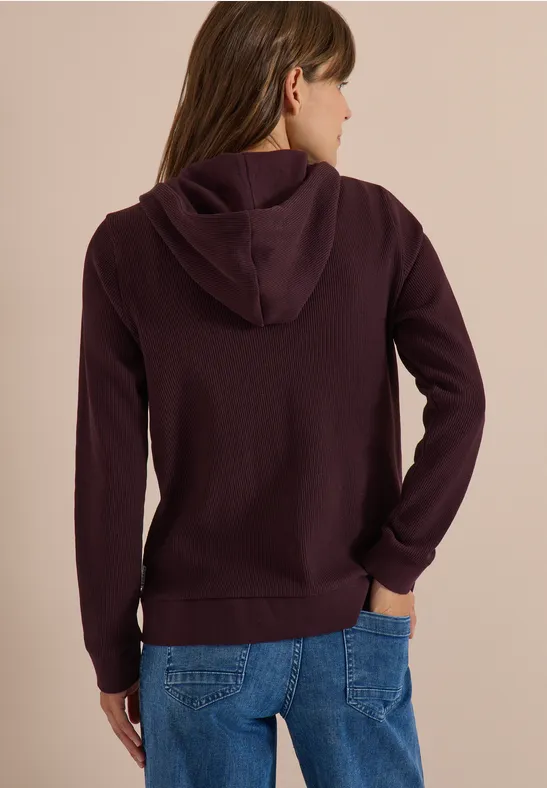 Persoon van achter gefotografeerd met een donkerpaarse capuchontrui en blauwe jeans.