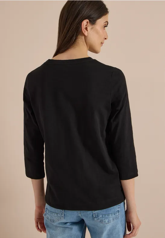 Achteraanzicht van een vrouw in een zwarte driekwartsmouwtop en jeans voor een lichte achtergrond.