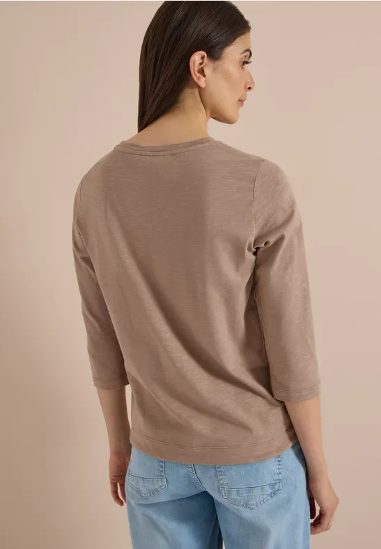 Frau von hinten, trägt beige 3/4-Arm-Pullover und helle Jeans.