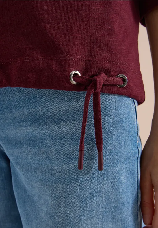 Een lichtblauwe jeans en een bordeauxrode trui met koordsluiting en zilverkleurige oogjes aan de zoom.
