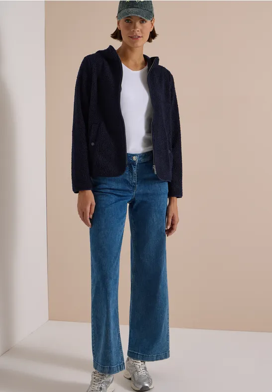 Frau mit Baseballcap, weißem T-Shirt, dunkelblauer Jacke, weitem Jeanshose und Sneakern