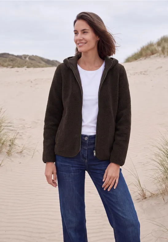 Vrouw in donkergroene fleecejas, wit t-shirt en blauwe jeans, glimlachend op het zandduin