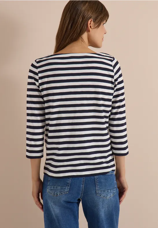 Rugaanzicht van een vrouw met gestreept driekwartsmouwshirt en blauwe jeans voor een lichte achtergrond.