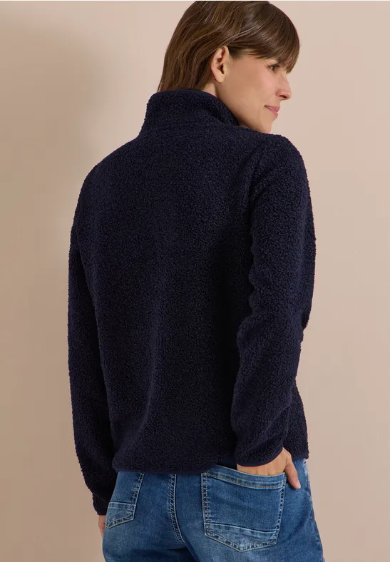 Frau von hinten in dunkelblauer Fleecejacke und Jeans vor neutralem Hintergrund.