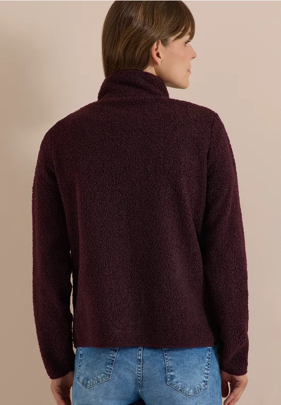 Rückansicht einer Frau in dunkelrotem, flauschigem Rollkragenpullover.