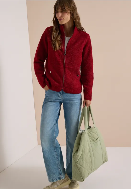 Frau trägt rote Fleecejacke, blaue Jeans und hält große grüne Stepp-Tasche.