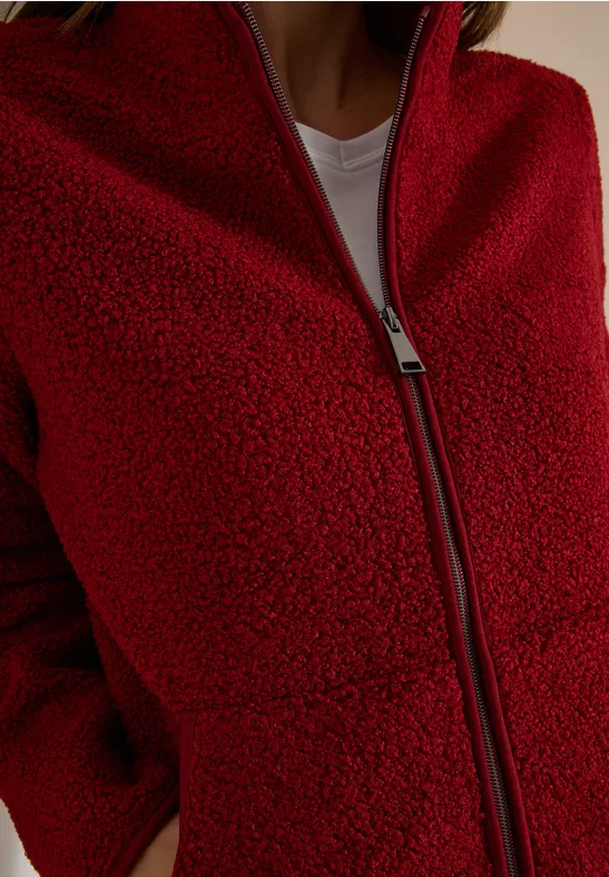Nahaufnahme einer roten Teddy-Fleecejacke mit Reißverschluss und seitlichen Taschen, weißes T-Shirt darunter.