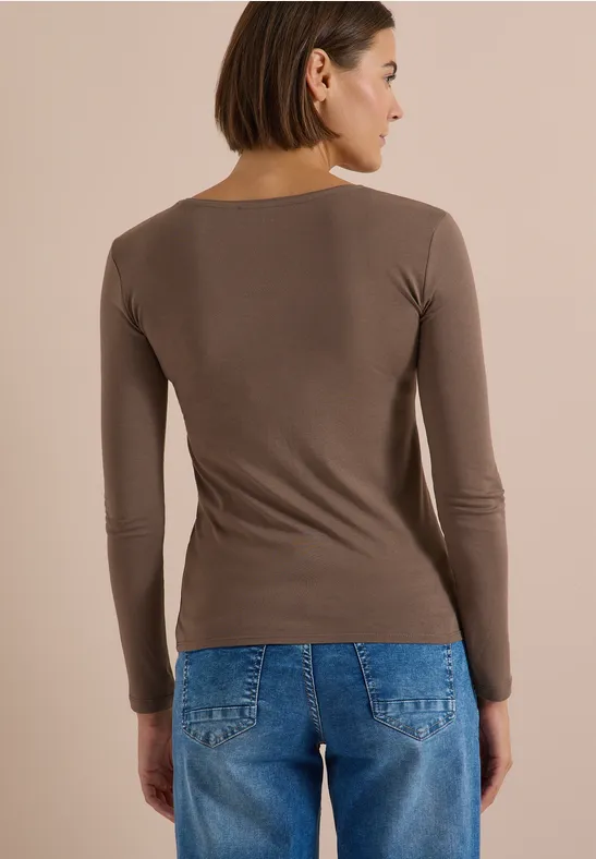 Vue de dos d'une femme portant un haut marron à manches longues et un jean bleu sur fond neutre.