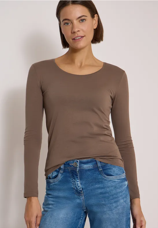 Femme en t-shirt marron moulant à manches longues et jean bleu sur fond neutre.