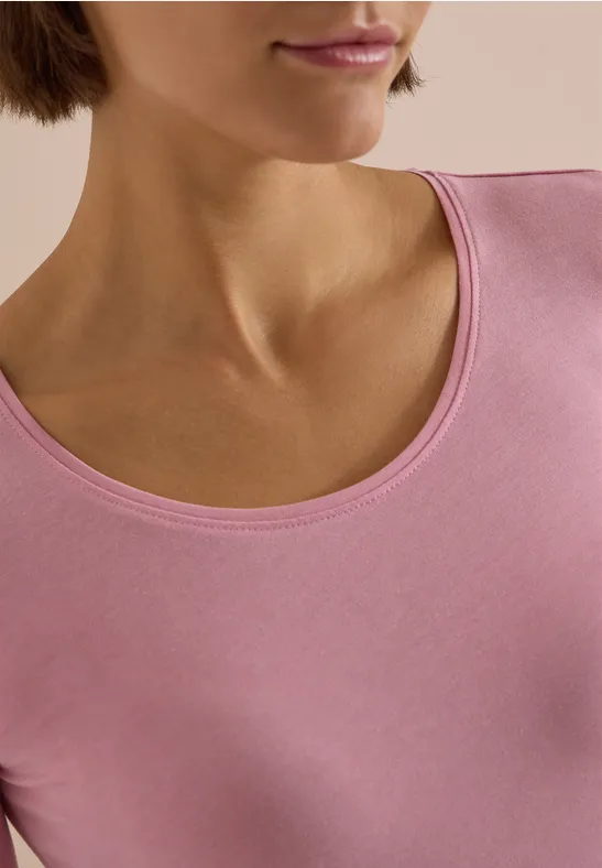 Gros plan sur le cou et le buste d’une personne portant un haut rose sur fond clair.