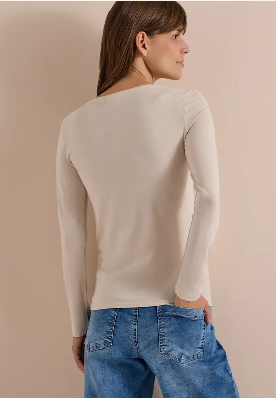 Rückansicht einer Frau mit beigem Langarmshirt und blauen Jeans.