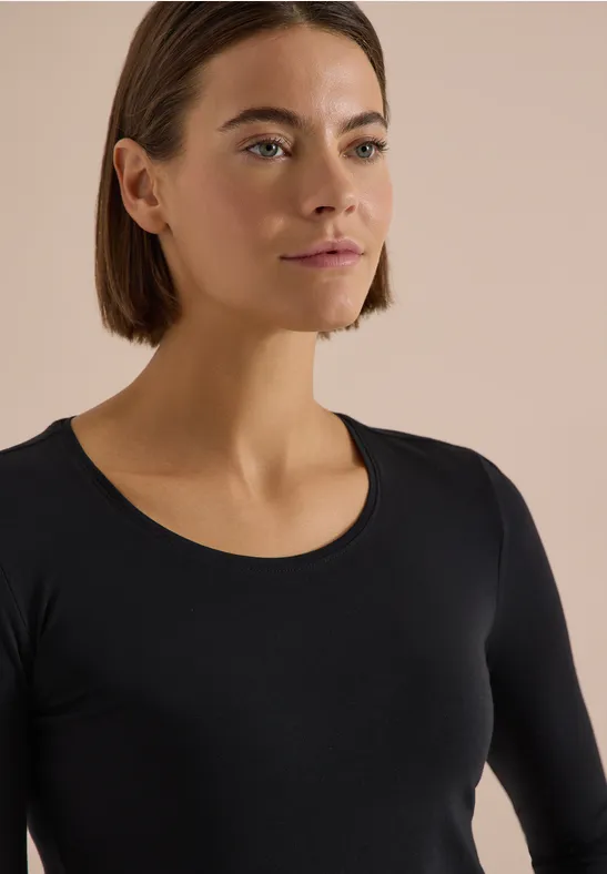 Femme aux cheveux bruns courts portant un haut noir à manches longues sur fond neutre.